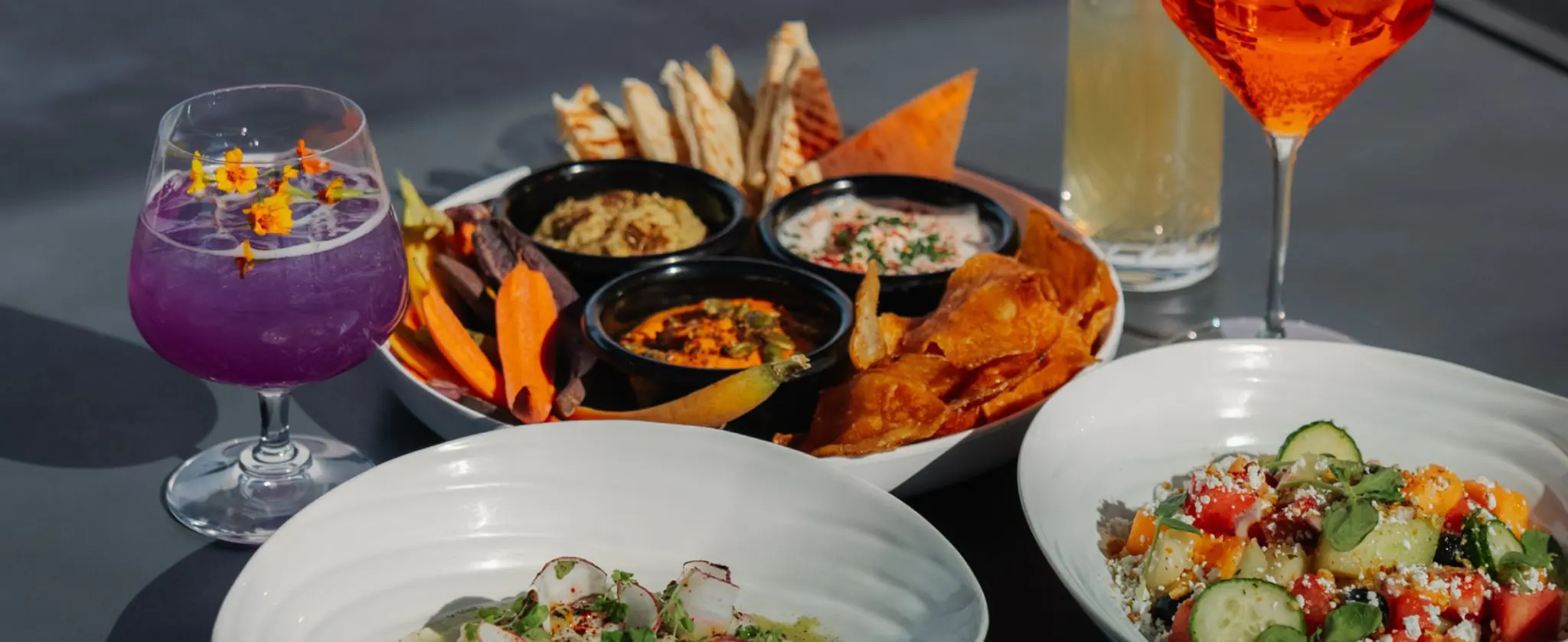 Colorful appetizer platter with dips, veggies, and cocktails on a table.