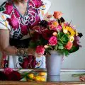 Woman arranging colorful flowers in a vase, wearing a vibrant embroidered dress.