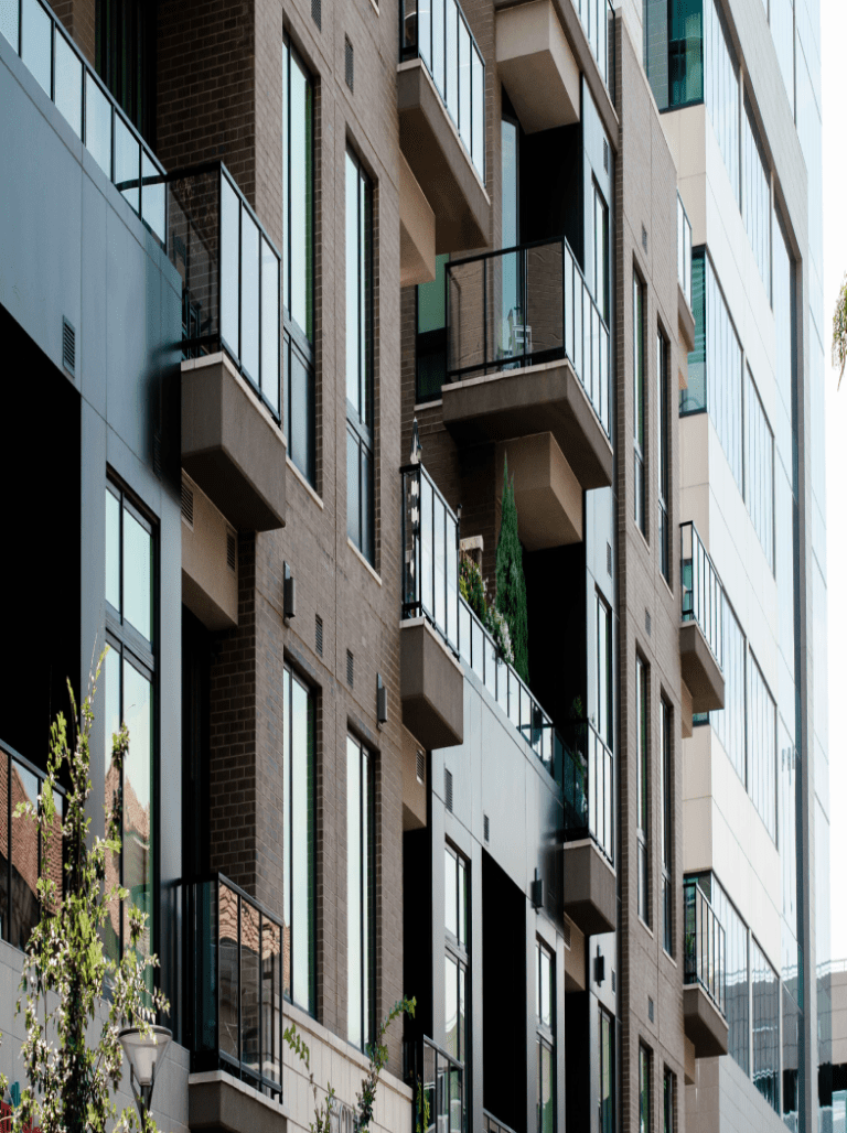 Modern brick apartment building with black trim and glass balconies in an urban setting.