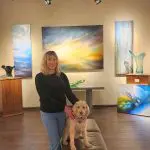 Sarah Parker of Masters Gallery with her dog, surrounded by art in a gallery setting.
