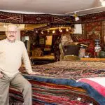 Man in Cherry Creek Oriental Rugs store with stacked rugs.