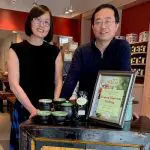 Ku Cha House of Tea owners stand in their Cherry Creek North store with tea and signage.