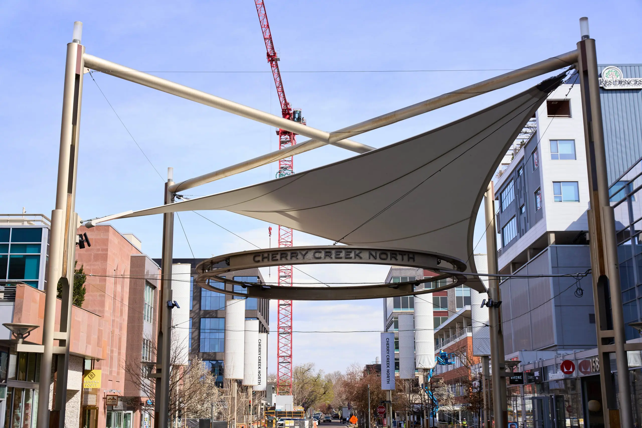 Cherry Creek North street view with modern architecture, construction crane, and overhead signage.