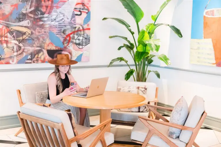 Woman in hat working on laptop in a boutique hotel lobby with modern art and furniture.