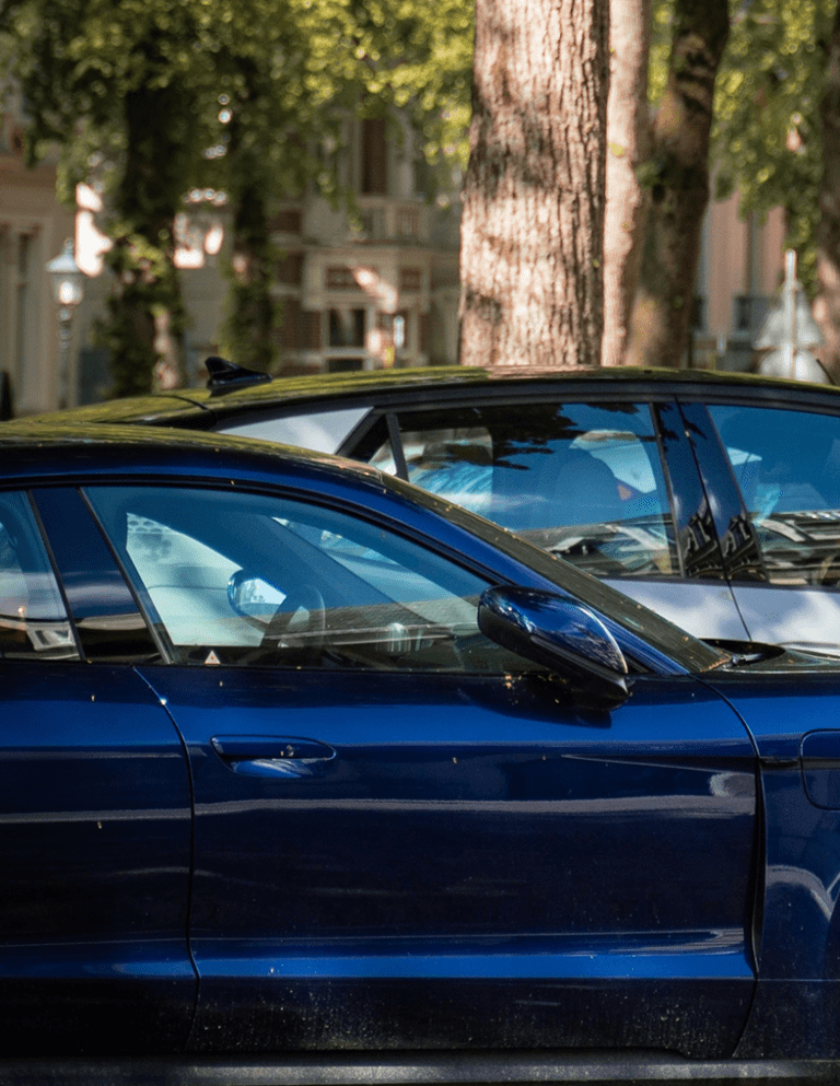 Dark blue car parked on a city street with trees and buildings in the background.
