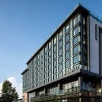 The Jacquard Hotel exterior with its modern glass and steel facade under a blue sky.