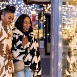 Two stylish women window shopping in Denver during winter, surrounded by festive lights.