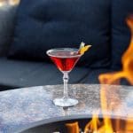 Cozy cocktail by a fire pit, perfect for staying cozy this season. Garnished with orange peel.