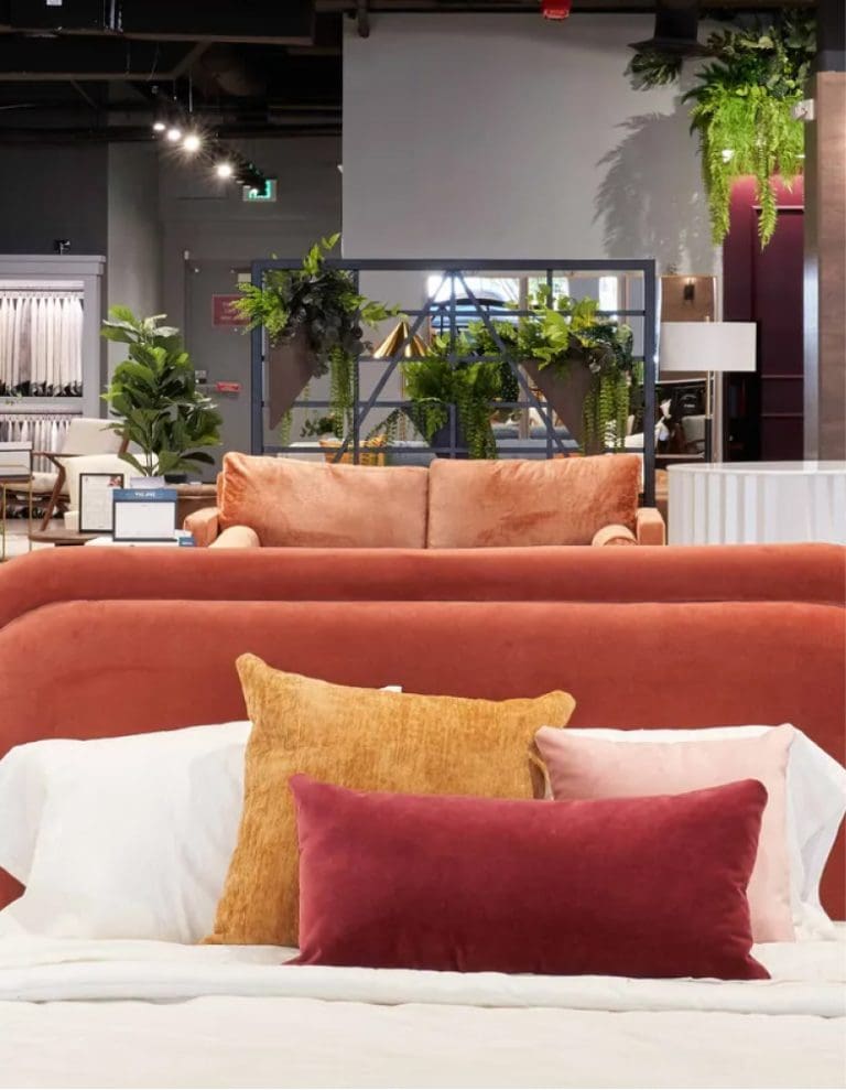 Stylish home decor featuring a velvet bed with colorful pillows and a glimpse of a modern living room setup.