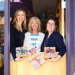 Three women stand in the Artisan Center doorway holding gifts.