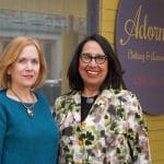 Two women stand in front of Adornments clothing store. Sign reads: "Adornments: Clothing & Accessories to Adore.