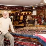 Man in Cherry Creek Oriental Rugs store with stacked rugs.