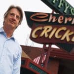Man stands in front of The Cherry Cricket sign. Denver restaurant.