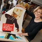 Woman at Gallerie Rouge holding a vintage war poster: "If you tell where he's going...