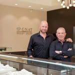 Gnat Jewelry Atelier owners standing in their jewelry store with display cases.