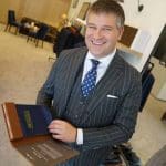 Man in a pinstripe suit holding an Icon Suit fabric sample book, smiling.