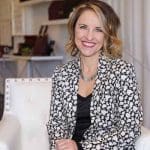 Keri Blair of The Style Studio, smiling in a black and white blazer, sitting in a white chair.