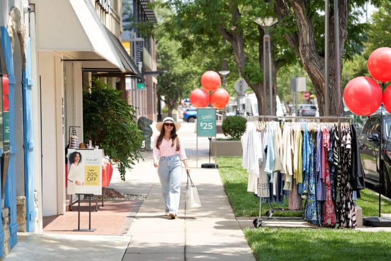 A woman walking down a side walk with clothes racks and balloons