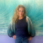 Alix Peterson, owner of Sinless Sun Spray Tanning, poses in front of a wave-like backdrop.